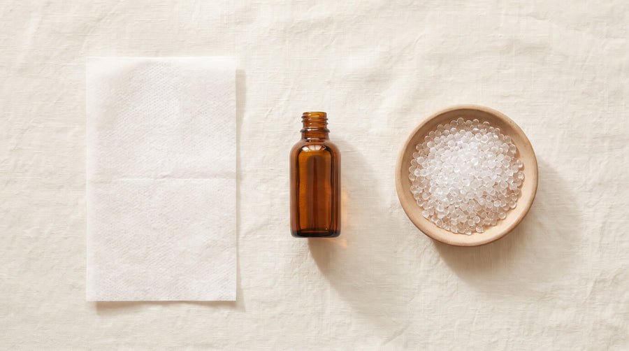 A dryer sheet, a bottle of liquid softener and a dish of scent beads laid out on linen